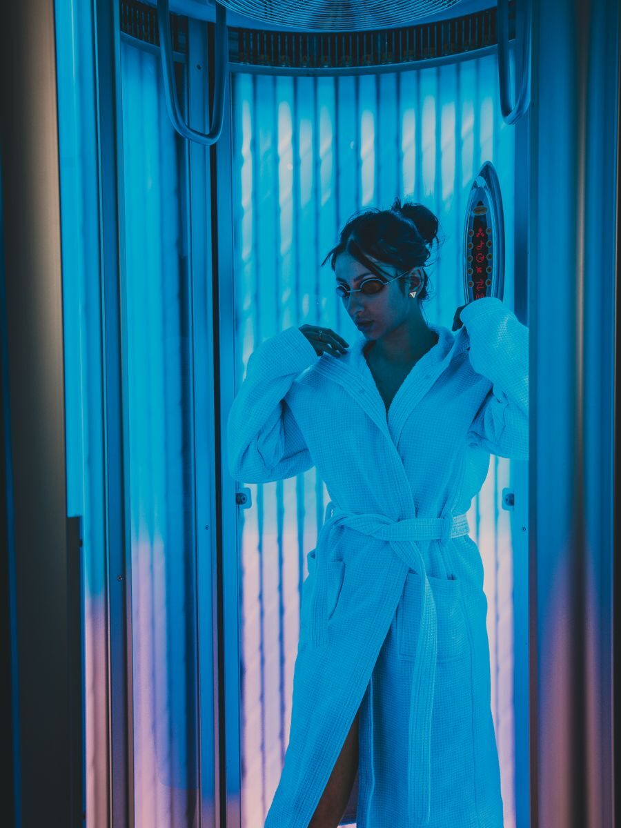 Woman wearing a bathrobe and eyeglasses inside a tanning booth at a beauty spa.